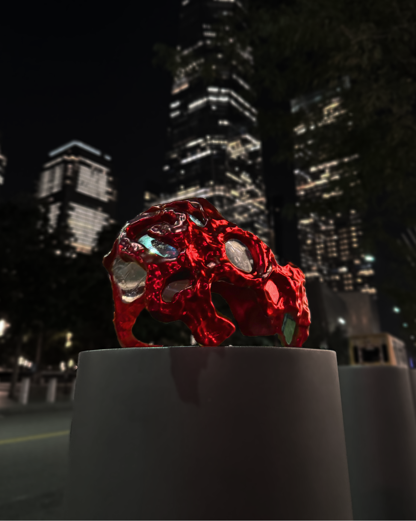 Red decorative object on a white pedestal against a city skyline at night