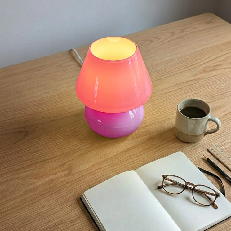 Colorful lamp on a wooden table with a notebook, glasses, and a mug.